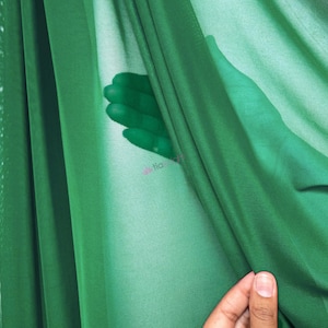 May include: A sheer, emerald green fabric with a fine mesh texture. The material is draped in soft folds, creating varying levels of opacity. The lightweight textile is translucent, allowing light to pass through and revealing a subtle texture.