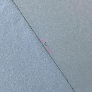 May include: A close-up shot of two fabric swatches in shades of blue. One swatch has a soft, fuzzy texture, while the other is smooth. The fabrics are divided diagonally, showcasing the contrast in textures and colors. The word "fia" is visible in pink.