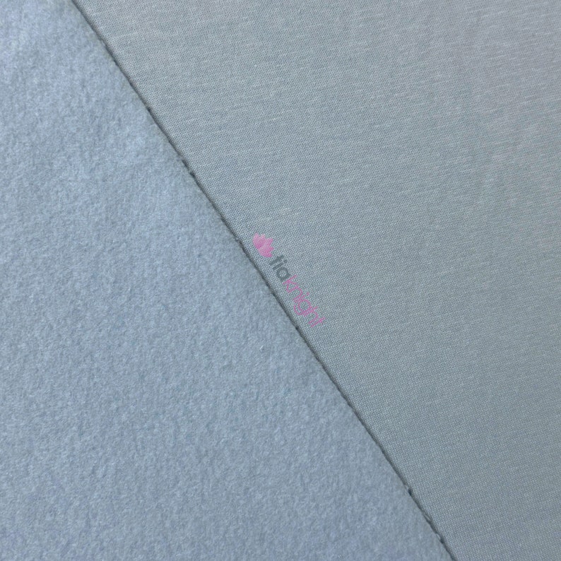 May include: A close-up shot of two fabric swatches in shades of blue. One swatch has a soft, fuzzy texture, while the other is smooth. The fabrics are divided diagonally, showcasing the contrast in textures and colors. The word "fia" is visible in pink.