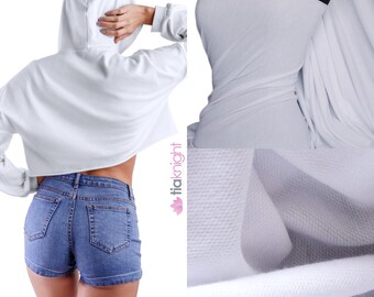 Op de afbeelding: Witte gecropte hoodie met een capuchon en lange mouwen. De hoodie is gemaakt van een zachte, rekbare stof. De stof wordt getoond in een close-up afbeelding.