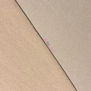 May include: A close-up shot of two fabric swatches. One swatch is a smooth, light tan color, while the other has a textured, beige appearance. A dark line separates the two fabrics, creating a diagonal division across the image.