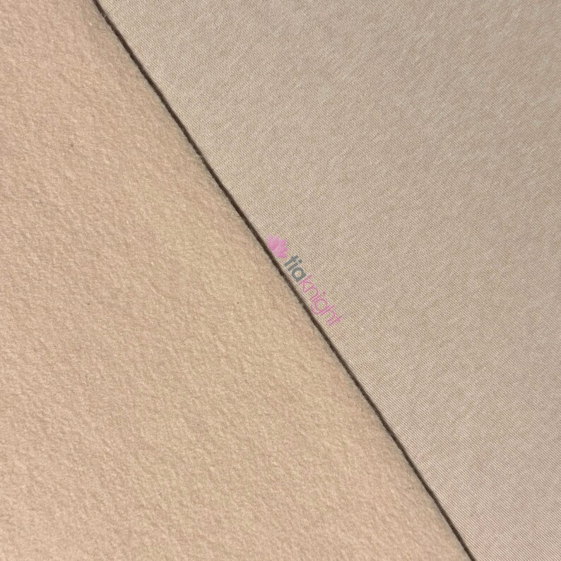 May include: A close-up shot of two fabric swatches. One swatch is a smooth, light tan color, while the other has a textured, beige appearance. A dark line separates the two fabrics, creating a diagonal division across the image.