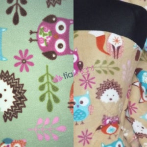 May include: Two fabric swatches featuring a woodland animal print. The left swatch has a light green background with pink flowers, brown branches, and owls. The right swatch has a beige background with brown branches, owls, hedgehogs, and birds.