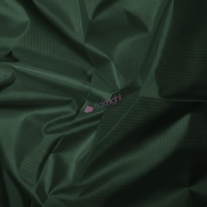 May include: Close-up of a dark green fabric with a subtle grid pattern. The material is folded, creating shadows and highlights that emphasize its texture. The fabric has a slight sheen, suggesting a smooth surface. The logo "tiaknight" is visible in the lower right corner.