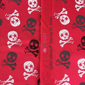 May include: Red fabric with a white and black skull and crossbones pattern. The fabric has the text "OuiTie Collection Oeko-Tex 100 Europe" printed on the side.