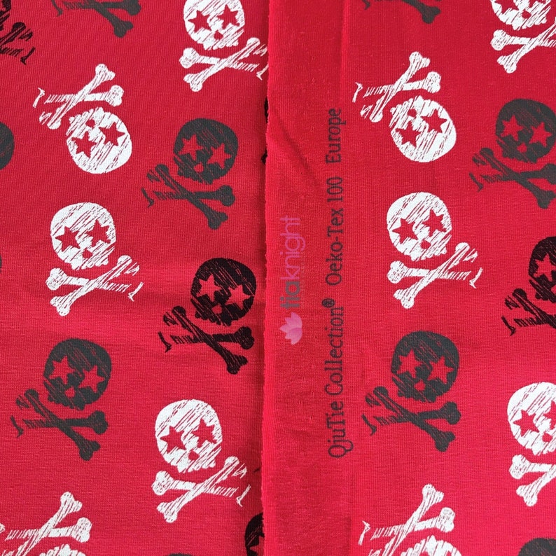 May include: Red fabric with a white and black skull and crossbones pattern. The fabric has the text "OuiTie Collection Oeko-Tex 100 Europe" printed on the side.