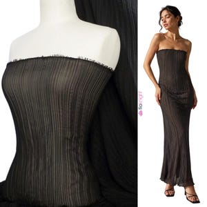 May include: A floor-length black strapless dress featuring a fine vertical pleated texture throughout the fabric. The garment has a straight neckline with a raw, frayed edge detail and a slim, column-like silhouette that extends to the ankles.
