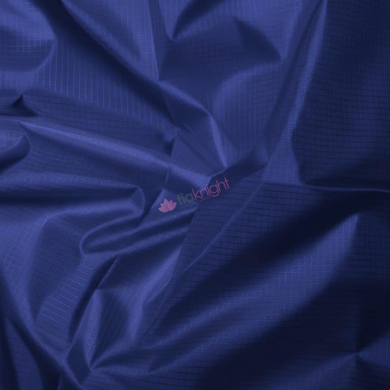 May include: Close-up of a deep blue fabric with a subtle grid pattern. The material has a slight sheen, with visible folds and creases adding texture. The fabric appears to be lightweight and possibly suitable for apparel or craft projects.
