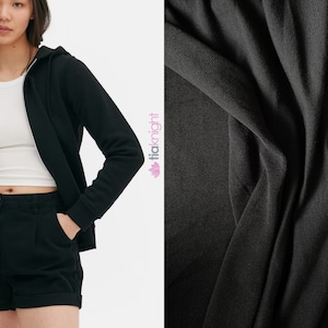 May include: A black zip-up hoodie with a hood and a white zipper. The hoodie is made of a soft, comfortable fabric. The fabric is shown in a close-up.