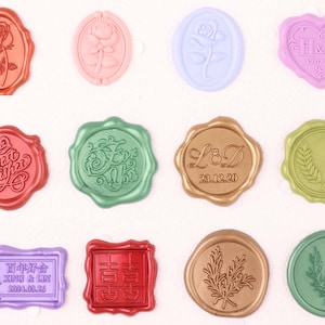 May include: A collection of colorful wax seals in various shapes, including ovals, hearts, and circles. Designs include roses, floral patterns, and text such as "Best Wishes" and initials with a date. The seals are in shades of pink, green, gold, and purple.