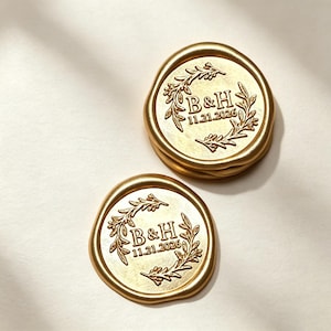 Peut inclure: Deux sceaux de cire dorés circulaires présentant un motif en relief composé d'une couronne de laurier entourant les lettres B&H et la date 11.21.2026. Les sceaux ont un bord irrégulier et organique ainsi qu'une finition métallique.