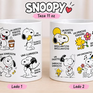 May include: Two white ceramic mugs featuring Snoopy and Woodstock illustrations with Spanish text. The mugs display various scenes including drinking coffee, hugging, talking on the phone, and listening to music. The text includes phrases like Un cafecito riquito, Un abracito, and Un rayito de sol. The mugs have a capacity of 11 oz.
