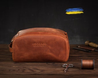 May include: A brown leather travel toiletry bag with a zipper closure and the text "VITTORIO SAPINO" embossed on the front.