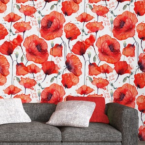 May include: A grey sofa with red and white cushions in front of a white wall with a red poppy floral pattern.