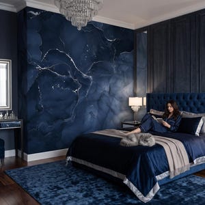 May include: A bedroom featuring a dark blue marble-patterned accent wall, a tufted navy blue upholstered bed with matching bedding, a beige throw blanket, a dark blue area rug, two bedside tables with crystal lamps, and a mirrored vanity table.