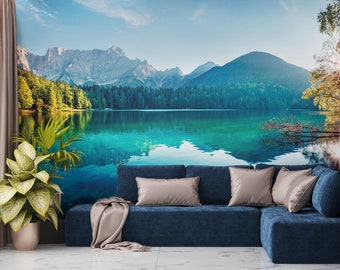 May include: A blue sectional sofa with a throw blanket sits in front of a wall mural depicting a lake surrounded by trees and mountains. The lake is a vibrant turquoise colour and the mountains are a soft blue.