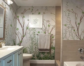 Puede incluir: Un baño con papel tapiz floral que presenta un árbol con flores blancas y hojas verdes. El baño tiene un lavabo de porcelana blanca, un inodoro blanco y una bañera blanca. El baño también tiene un suelo de baldosas marrones y una ducha de baldosas marrones.