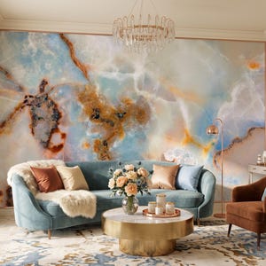 May include: A large wall mural featuring a swirling blue, white, and amber marble pattern. The room includes a curved light blue sofa with various throw pillows, a round gold coffee table, a brown armchair, and a crystal chandelier overhead.