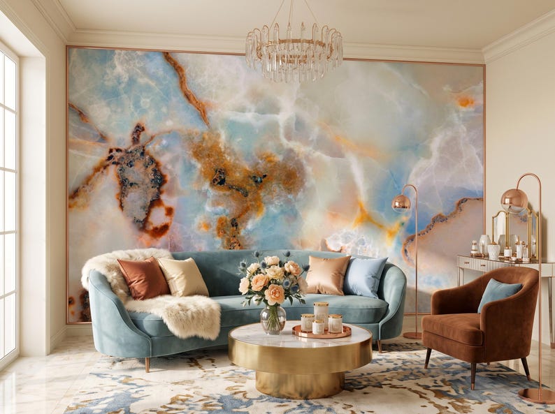 May include: A large wall mural featuring a swirling blue, white, and amber marble pattern. The room includes a curved light blue sofa with various throw pillows, a round gold coffee table, a brown armchair, and a crystal chandelier overhead.