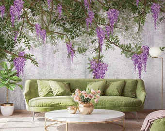 May include: A green velvet sofa with pillows sits in front of a wall with a mural of purple wisteria flowers hanging from branches. A vase of pink flowers sits on a round coffee table in front of the sofa.