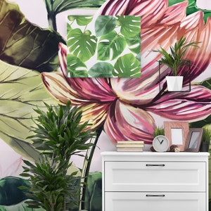Pu&ograve; includere: Un vivace murale floreale con grandi fiori e foglie rosa e verdi. Una piccola tela incorniciata con foglie verdi di monstera &egrave; montata sulla parete. Un com&ograve; bianco contiene un orologio, cornici e una piccola pianta in vaso.
