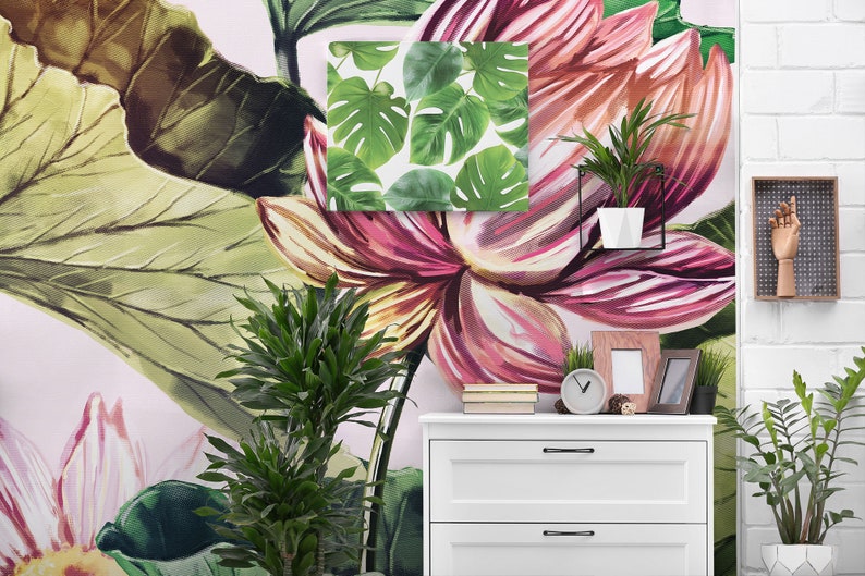 Pu&ograve; includere: Un vivace murale floreale con grandi fiori e foglie rosa e verdi. Una piccola tela incorniciata con foglie verdi di monstera &egrave; montata sulla parete. Un com&ograve; bianco contiene un orologio, cornici e una piccola pianta in vaso.
