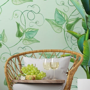 Puede incluir: Una silla de mimbre con un cojín blanco y una bandeja con uvas y queso. Dos copas de vino blanco están en la bandeja. La silla está frente a una pared verde con un patrón de vid frondosa.