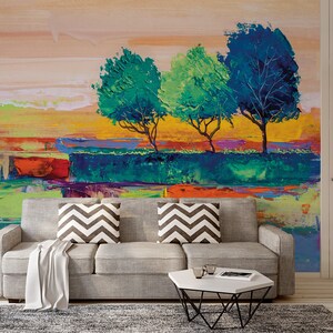 Może przedstawiać: Abstrakcyjne malarstwo przedstawiające krajobraz z trzema drzewami w odcieniach zieleni i błękitu na tle ż&oacute;łtym, pomarańczowym i r&oacute;żowym. Obraz jest umieszczony na ścianie w salonie z szarą sofą i białym stolikiem kawowym.
