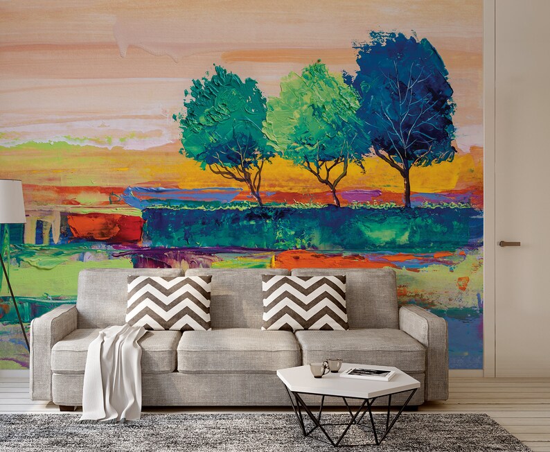 Może przedstawiać: Abstrakcyjne malarstwo przedstawiające krajobraz z trzema drzewami w odcieniach zieleni i błękitu na tle ż&oacute;łtym, pomarańczowym i r&oacute;żowym. Obraz jest umieszczony na ścianie w salonie z szarą sofą i białym stolikiem kawowym.