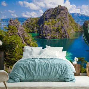 May include: A bedroom with a bed and a white chair. The wall behind the bed is a mural of a tropical island with a blue lagoon and green cliffs.
