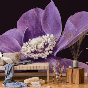 May include: A white dog sits on a wooden bench in front of a large purple flower with a dark background.