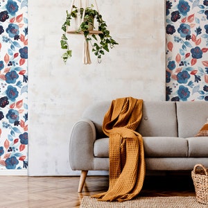 Puede incluir: Un sofá gris con una manta de color amarillo mostaza y dos almohadas. El sofá está frente a una pared con fondo blanco y un patrón de papel tapiz floral azul y rojo.