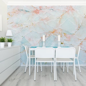 May include: A white dining table with four white chairs and a blue runner. The wall behind the table is covered in a marble-patterned wallpaper with pink, blue, and gold accents.