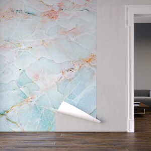 May include: A close-up of a peel-and-stick wallpaper with a light blue, white, and pink marble pattern. The wallpaper is being applied to a white wall in a room with a wooden floor.