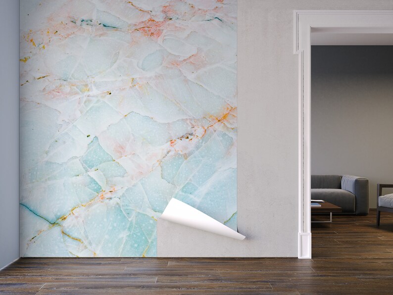 May include: A close-up of a peel-and-stick wallpaper with a light blue, white, and pink marble pattern. The wallpaper is being applied to a white wall in a room with a wooden floor.