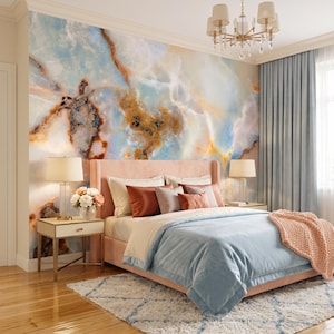 May include: A bedroom featuring a large wall mural with a blue, white, and amber marble pattern. A pink upholstered bed is dressed with light blue bedding, a peach knit throw, and various pillows. Two bedside tables hold lamps and flowers.