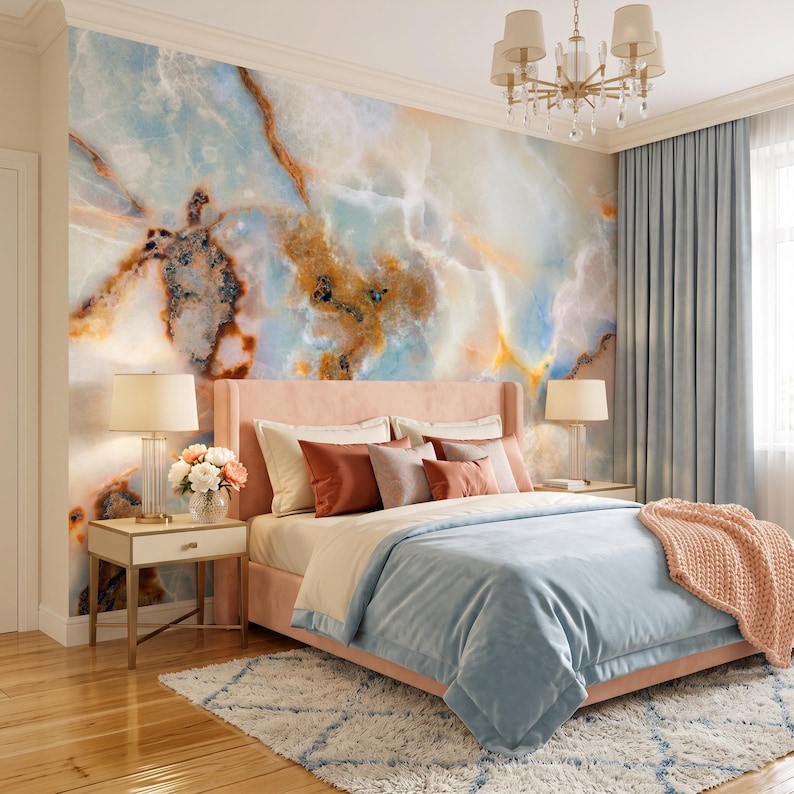 May include: A bedroom featuring a large wall mural with a blue, white, and amber marble pattern. A pink upholstered bed is dressed with light blue bedding, a peach knit throw, and various pillows. Two bedside tables hold lamps and flowers.