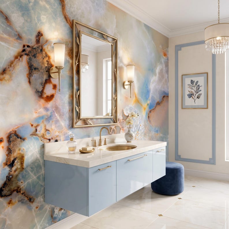 May include: A bathroom vanity with a light blue cabinet, a white countertop, and a gold faucet. Above the vanity is a rectangular mirror with a gold frame, flanked by two gold wall sconces. The wall features a blue and brown marble pattern.