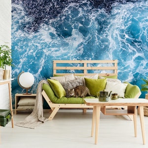 Może przedstawiać: Salon z zieloną sofą i drewnianym stolikiem kawowym. Ściana za sofą to mural przedstawiający niebieskie fale oceanu z białą pianą.