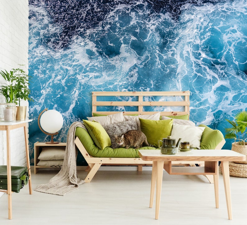 Może przedstawiać: Salon z zieloną sofą i drewnianym stolikiem kawowym. Ściana za sofą to mural przedstawiający niebieskie fale oceanu z białą pianą.