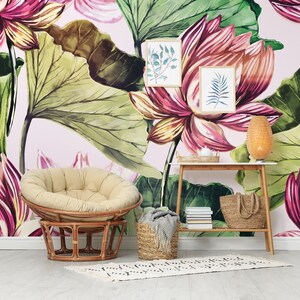 Pu&ograve; includere: Una stanza con carta da parati floreale con grandi fiori di loto rosa e verdi. Una sedia in rattan con un cuscino beige &egrave; di fronte al muro. Un tavolino in legno contiene una lampada intrecciata, stampe botaniche incorniciate e un cesto intrecciato.