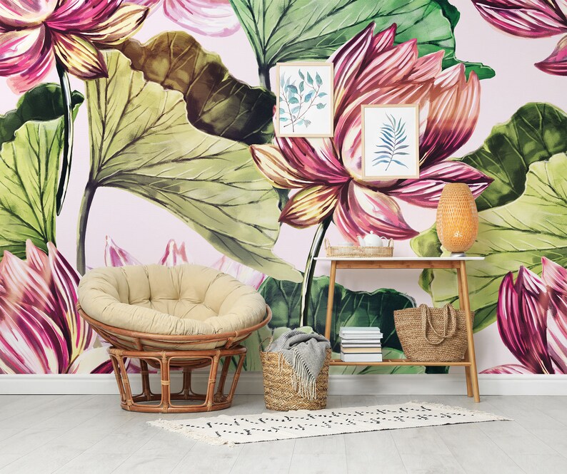 Pu&ograve; includere: Una stanza con carta da parati floreale con grandi fiori di loto rosa e verdi. Una sedia in rattan con un cuscino beige &egrave; di fronte al muro. Un tavolino in legno contiene una lampada intrecciata, stampe botaniche incorniciate e un cesto intrecciato.