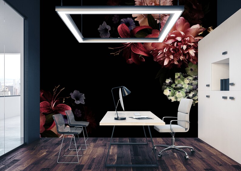 May include: A modern office space with a black wall featuring a floral mural. The mural features red, pink, and green flowers on a black background. A white desk with a black chair and a lamp sits in front of the mural.