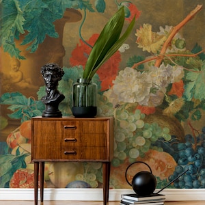 Può includere: Un dipinto di natura morta vintage che rappresenta un vaso di fiori, frutta e uva. Il dipinto è esposto su una parete dietro una cassettiera in legno con tre cassetti. Una scultura nera di busto è sopra la cassettiera. Un annaffiatoio nero e una pila di libri sono sul pavimento davanti alla cassettiera.
