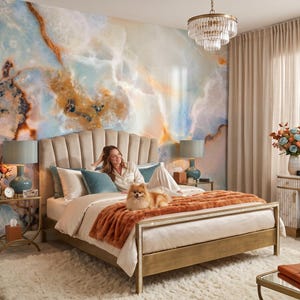 May include: A bedroom featuring a scalloped beige upholstered bed frame with a plush orange throw blanket, set against a large-scale wall mural with blue, white, and amber marble patterns, complemented by a crystal chandelier and two bedside lamps.