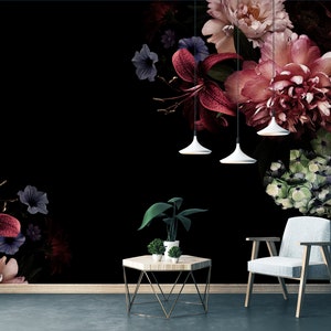 May include: A black and white floral wallpaper with a dark red, pink, and green floral pattern. A white chair and a wooden table with a gold metal base are in front of the wallpaper.