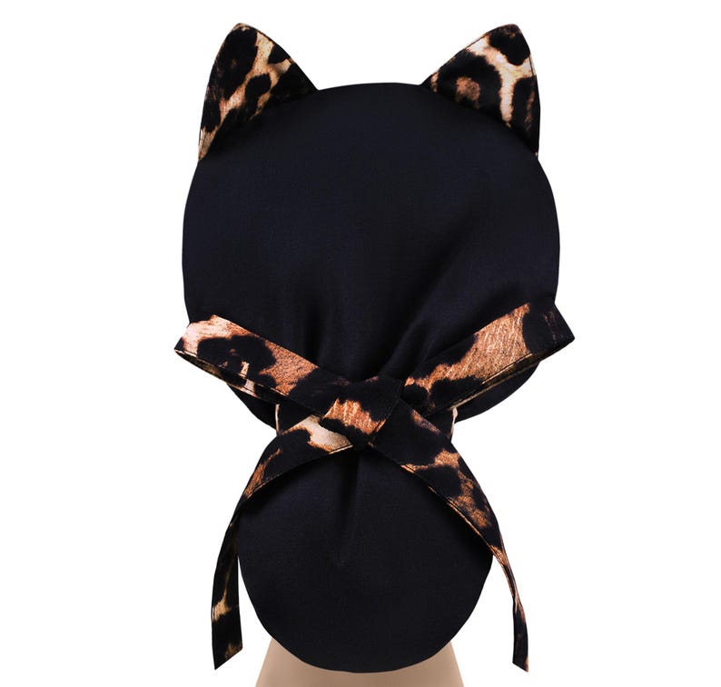 May include: Black cat ear hat with a leopard print accent on the ears and bow. The hat is made of a soft, dark fabric and features a playful design. The bow is tied at the back, adding a decorative touch.