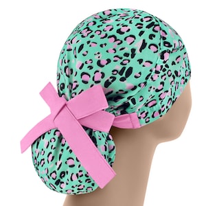 May include: A green and pink leopard print surgical scrub hat with a pink bow at the back.