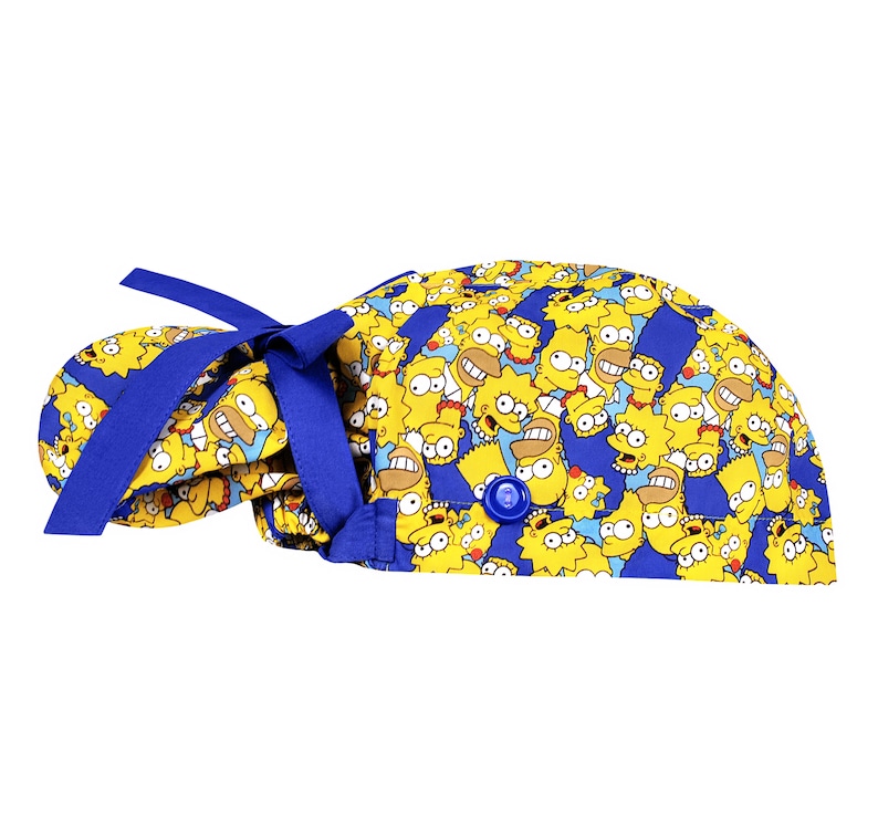 Puede incluir: Un gorro de quir&oacute;fano azul y amarillo con un patr&oacute;n de personajes de dibujos animados de Los Simpson. El gorro tiene una corbata azul y un bot&oacute;n en la parte superior.
