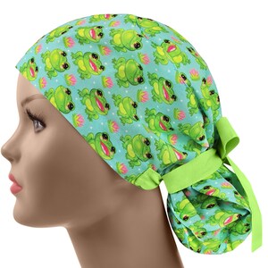 May include: A light blue scrub cap featuring a repeating pattern of smiling green frogs and pink water lilies. The cap has a lime green tie in the back. The cap is designed to be worn on the head.